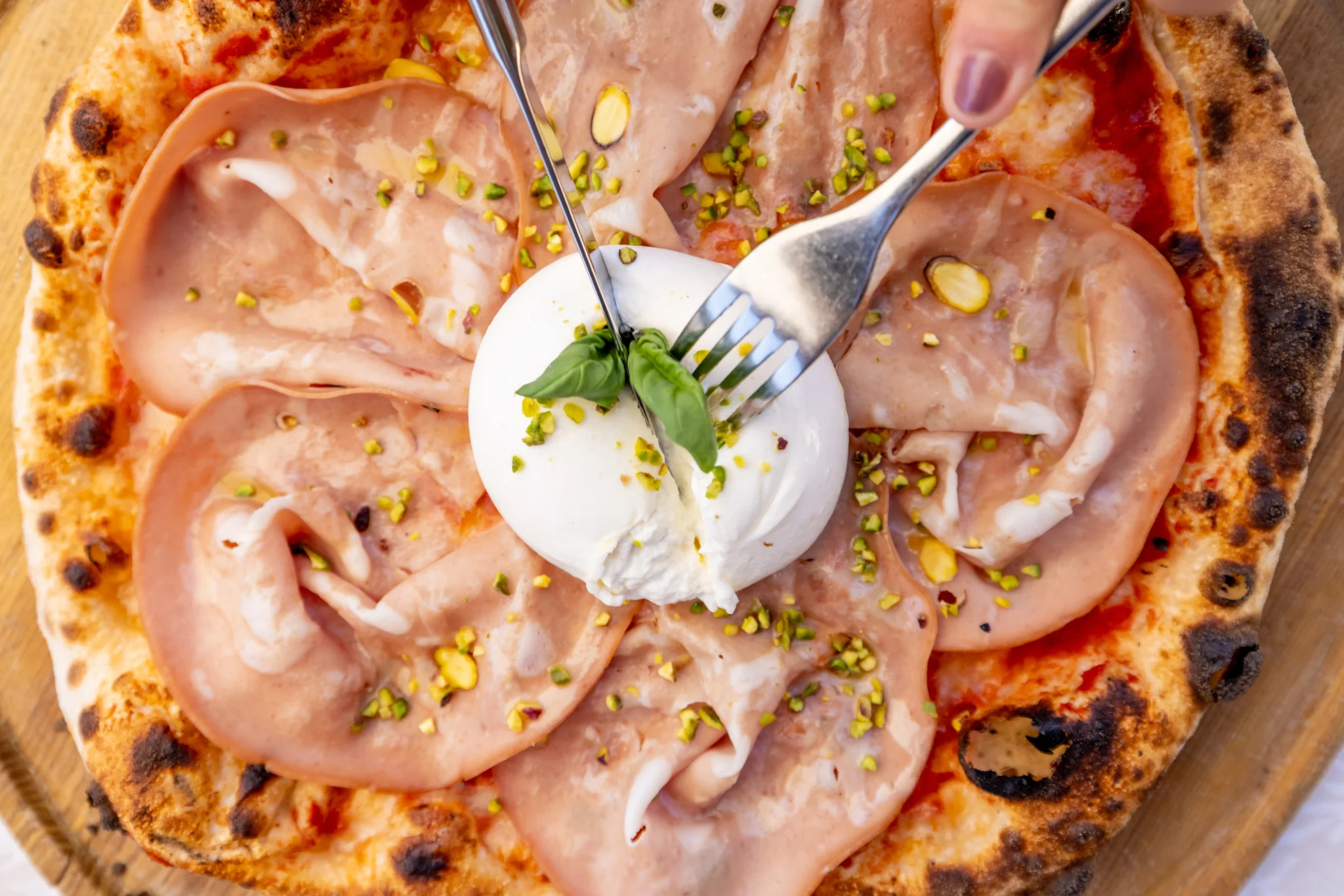 Pizza con prosciutto cotto, burrata cremosa e granella di pistacchio, cotta nel forno a legna