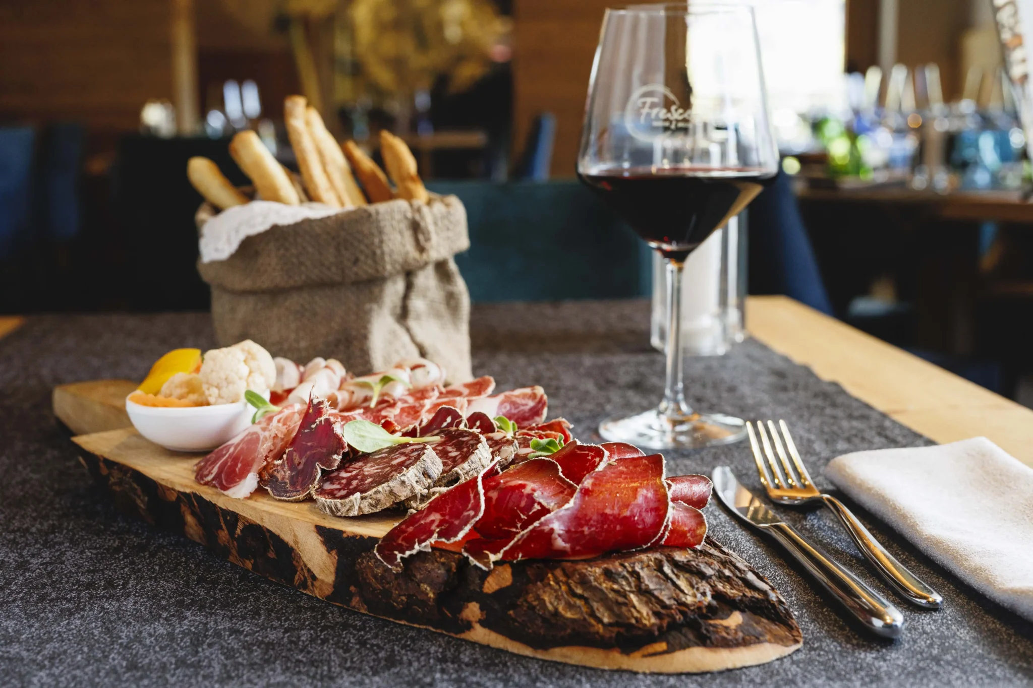 Tagliere di salumi con formaggio e calice di vino rosso, servito su tavolo elegante a Livigno