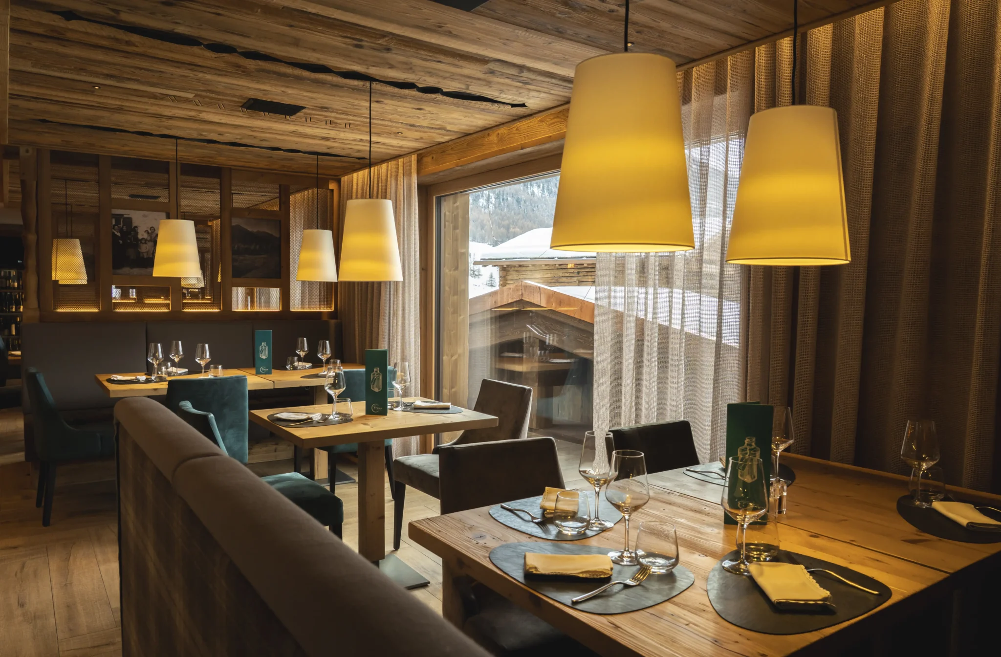 Ristorante elegante in legno con tavoli apparecchiati e lampade calde, vista sulle montagne di Livigno