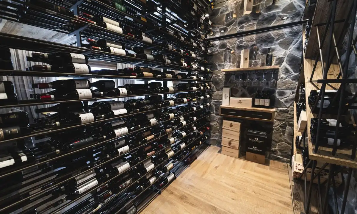 Cantina dei vini dell'hotel con scaffali a vista e parete in pietra, atmosfera calda per coppie