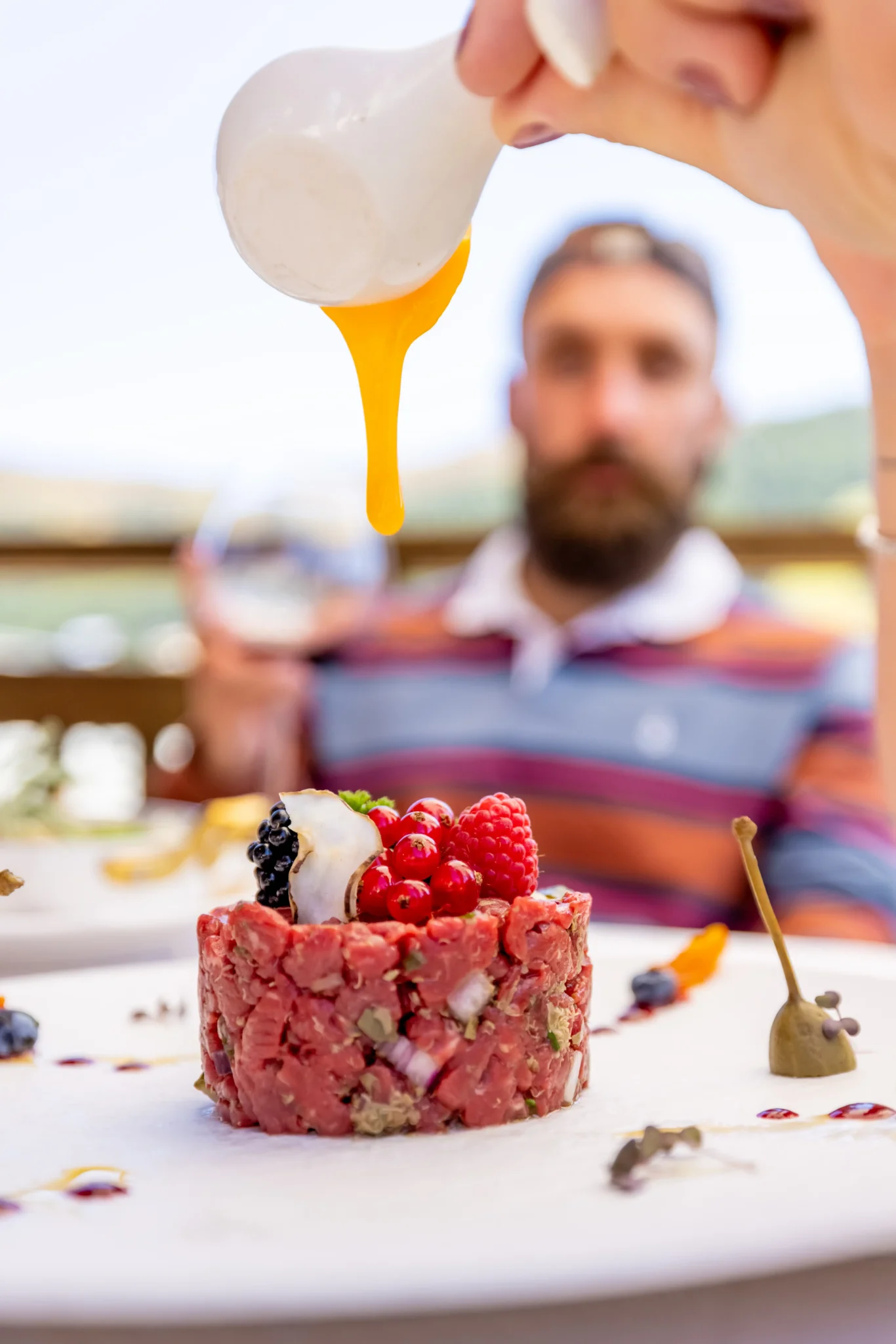 Tartare di carne con lamponi mentre viene versato un tuorlo d'uovo, con montagne sullo sfondo