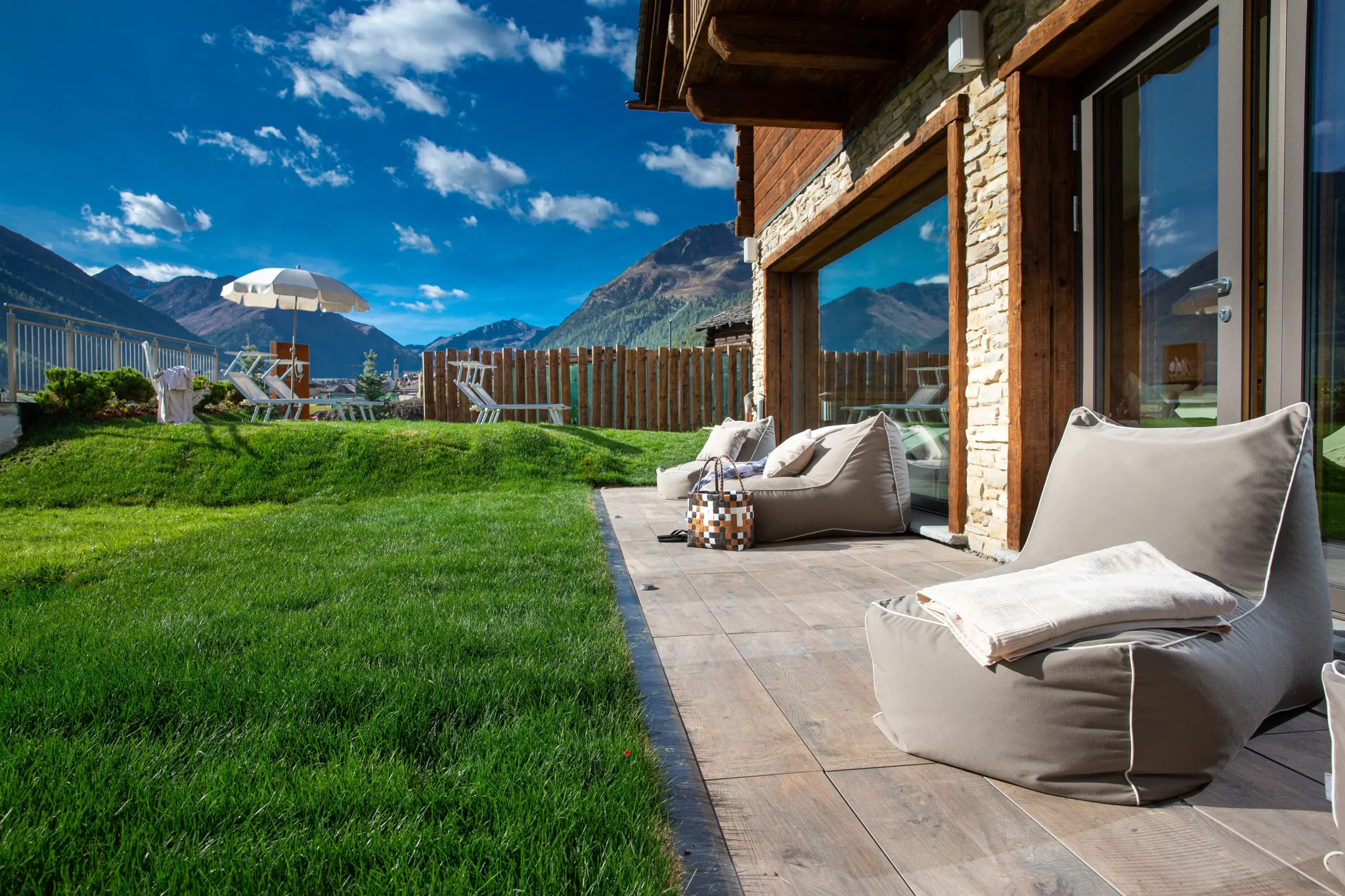 Terrazza dell'hotel con pouf beige, prato verde e vista sulle montagne di Livigno