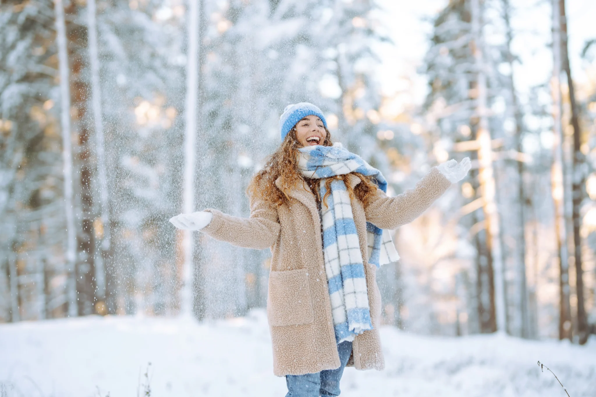 Donna sorridente gioca con la neve tra gli alberi innevati durante una vacanza invernale a Livigno