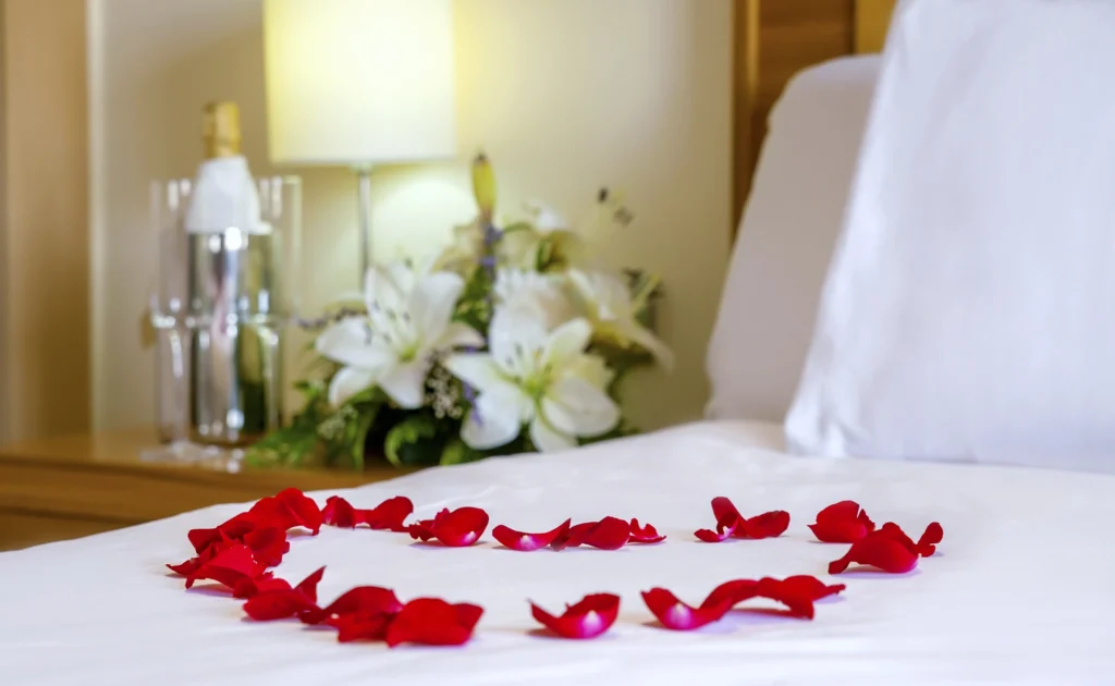Petali di rosa rossi a forma di cuore sul letto con gigli bianchi, allestimento romantico per coppie