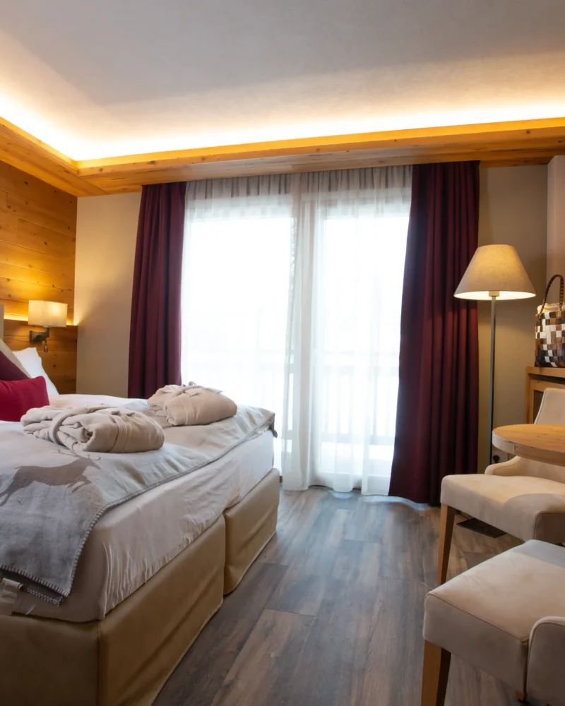Camera doppia in legno con letto matrimoniale, tavolino e balcone in hotel a Livigno