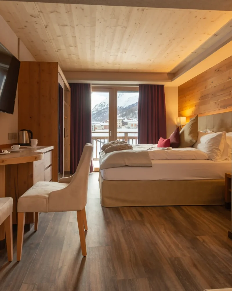 Camera d'hotel elegante in legno con letto matrimoniale, TV e vista sulle montagne di Livigno