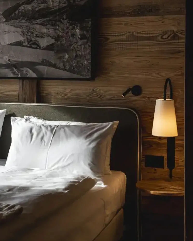 Camera in legno con letto soffice e lampada calda da comodino, atmosfera romantica per coppie a Livigno