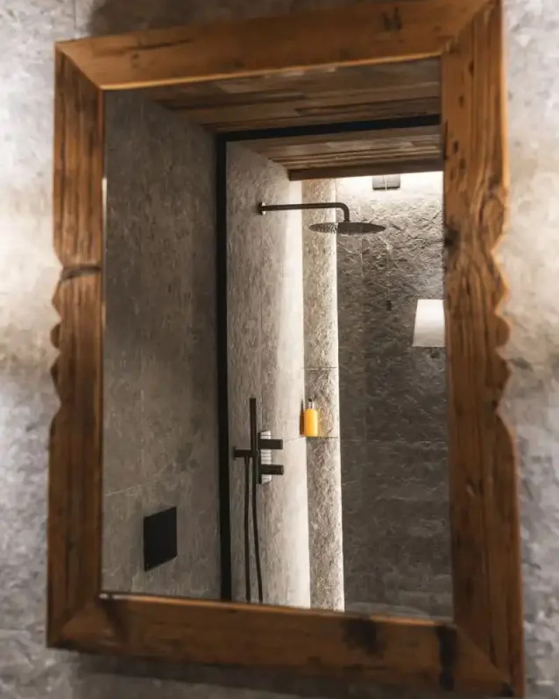 Specchio in legno rustico riflette doccia in pietra di un elegante bagno hotel a Livigno