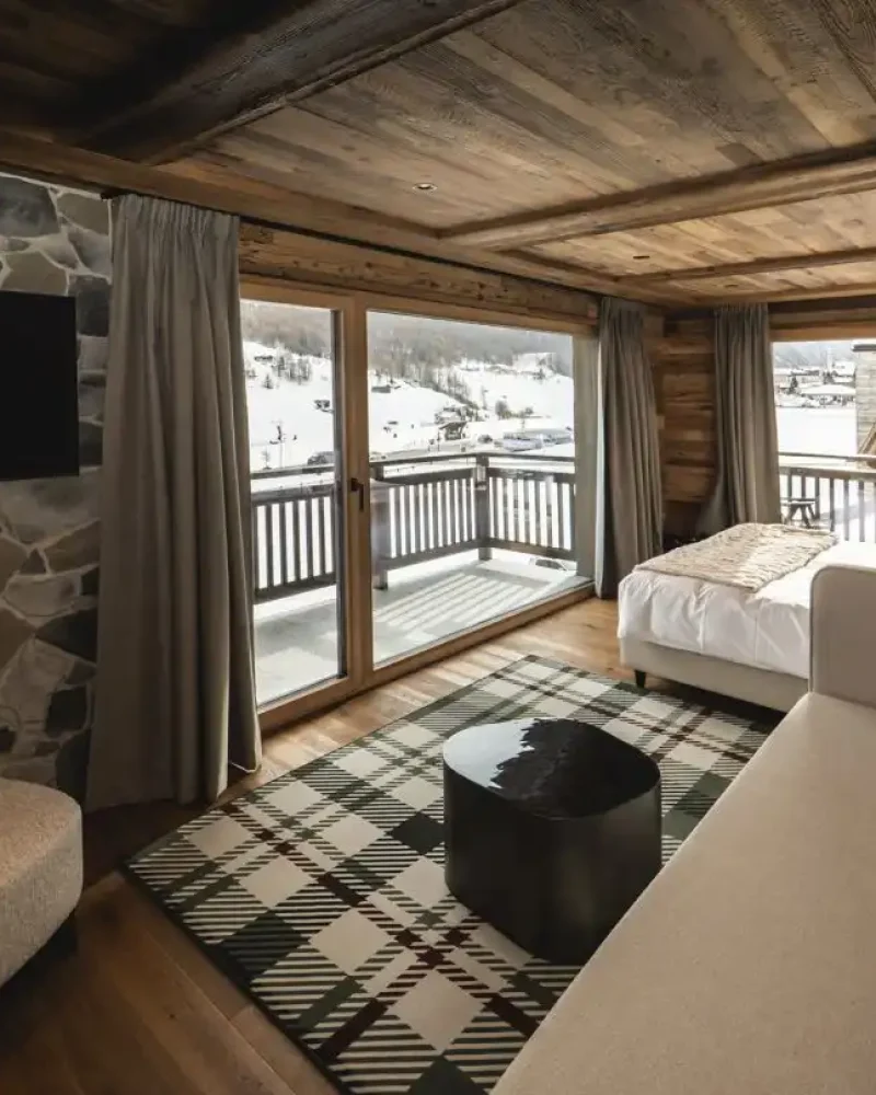 Camera in stile chalet con letto, divano panoramico e vista sulle montagne di Livigno