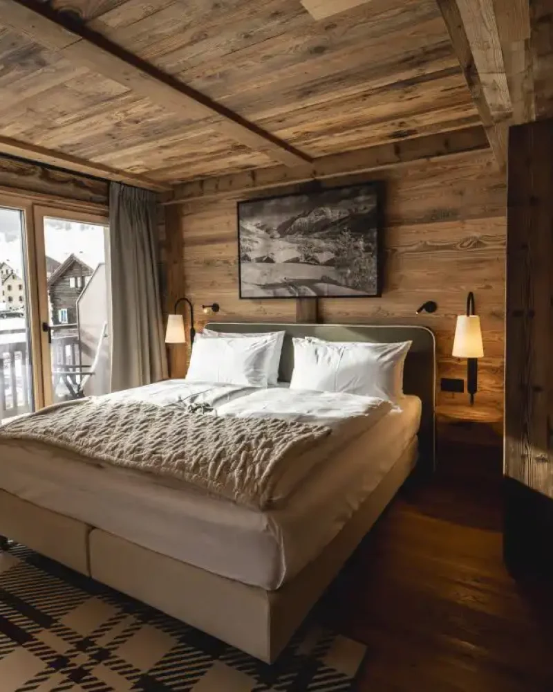 Camera in legno con letto matrimoniale, luci soffuse e balcone affacciato sulle montagne di Livigno