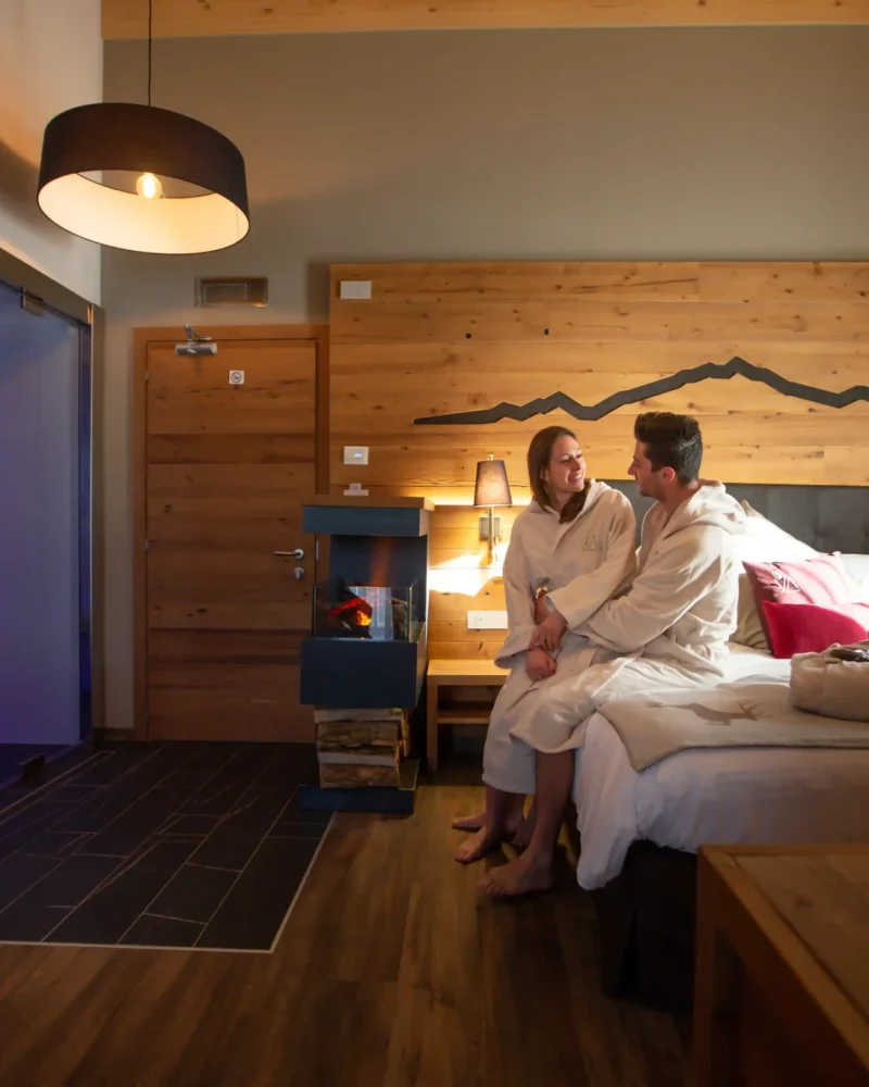 Coppia in accappatoio seduta sul letto in camera d'hotel con parete in legno a Livigno