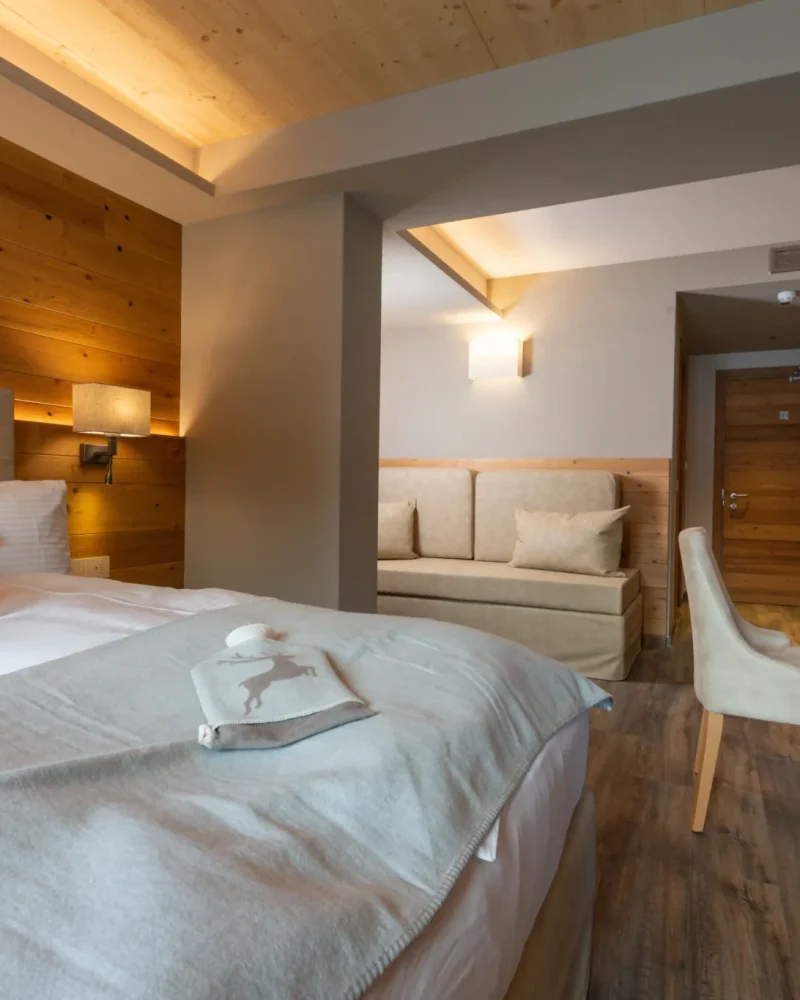 Camera d'hotel elegante con letto matrimoniale, divano e arredi in legno a Livigno