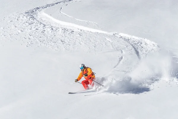 Sciatore in tuta arancione scende tra la neve fresca fuoripista sulle montagne di Livigno