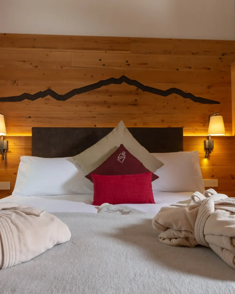 Camera in legno con letto matrimoniale, cuscino rosso e accappatoi soffici, atmosfera calda e romantica
