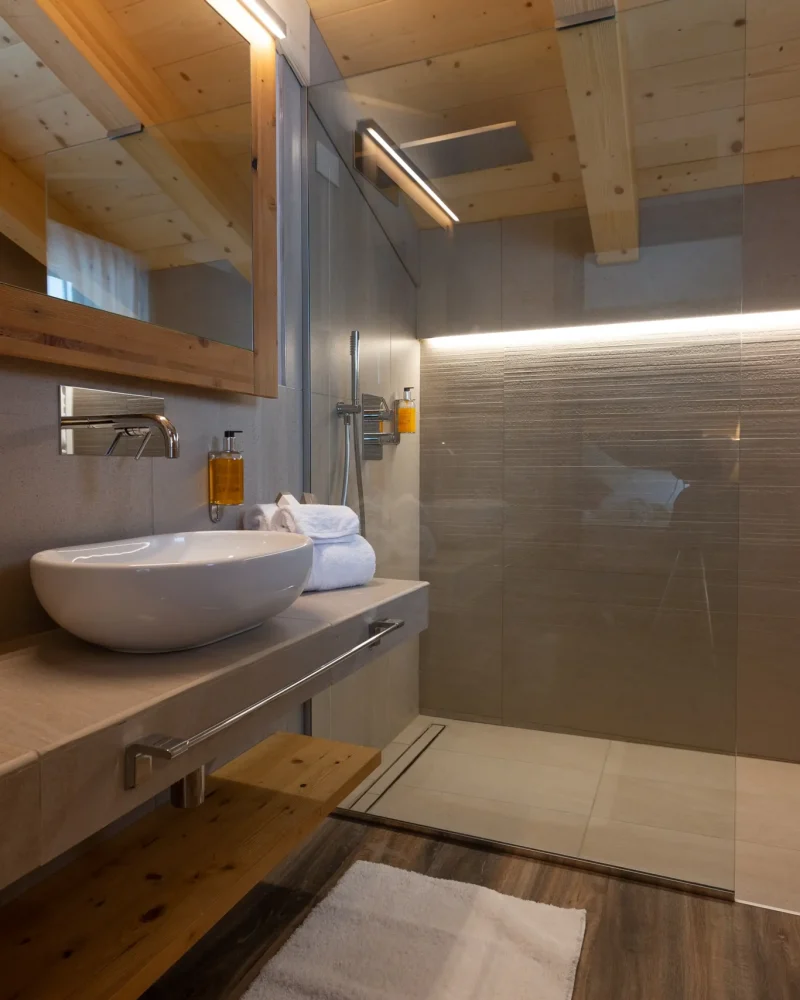 Bagno elegante in legno con lavabo d'appoggio e doccia in vetro illuminata a Livigno