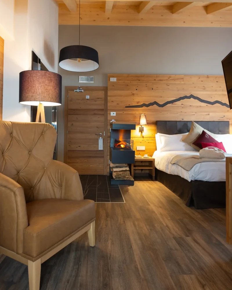Camera d'albergo elegante in stile chalet con letto matrimoniale, poltrona e camino a Livigno