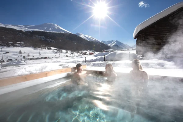 Persone rilassate nella vasca idromassaggio esterna con vista sulle montagne innevate di Livigno